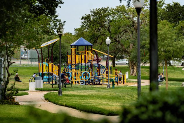 Children playing on a large playground set in a city park.