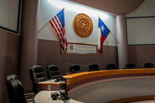 Empty council chambers podium with flags and seal in the background.