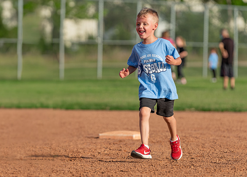 young child smiling and running between bases on a baseball diamond