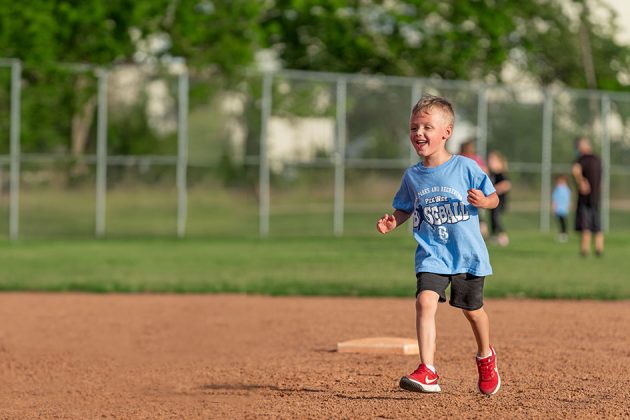 young child smiling and running between bases on a baseball diamond