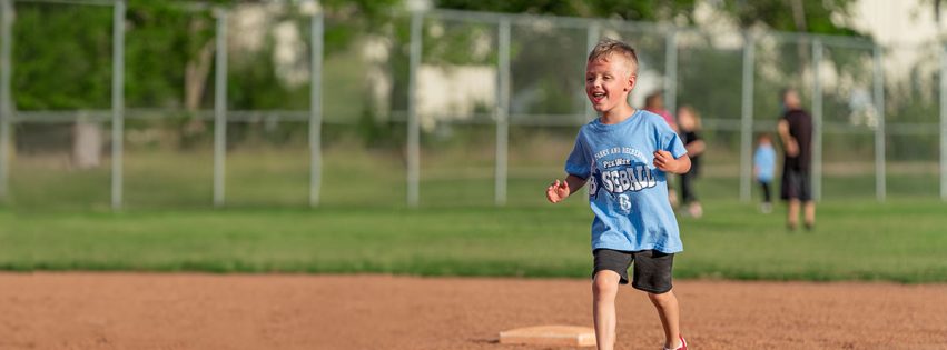 young child smiling and running between bases on a baseball diamond