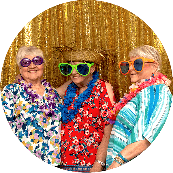 seniors posing for a photo booth on a sparkly gold backdrop wearing oversized prop sunglasses and colorful leis