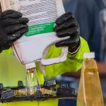 Staff member wearing protective gear pouring hazardous bottle of liquid into a waste receptacle