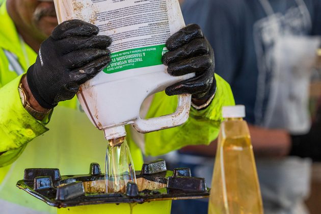 Staff member wearing protective gear pouring hazardous bottle of liquid into a waste receptacle