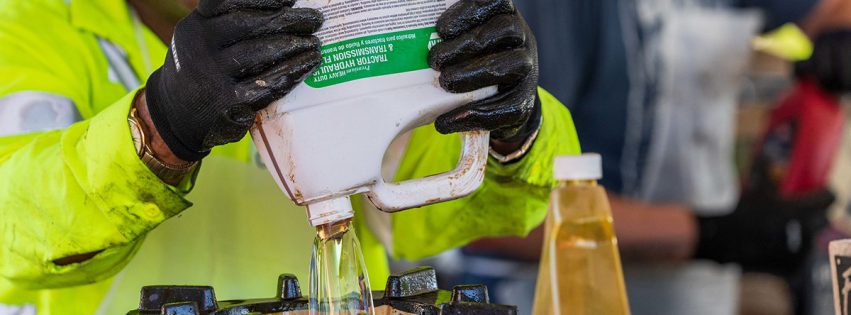 Staff member wearing protective gear pouring hazardous bottle of liquid into a waste receptacle