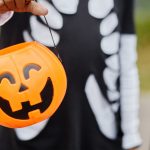 child in halloween costume holding a jack-o-lantern candy bucket