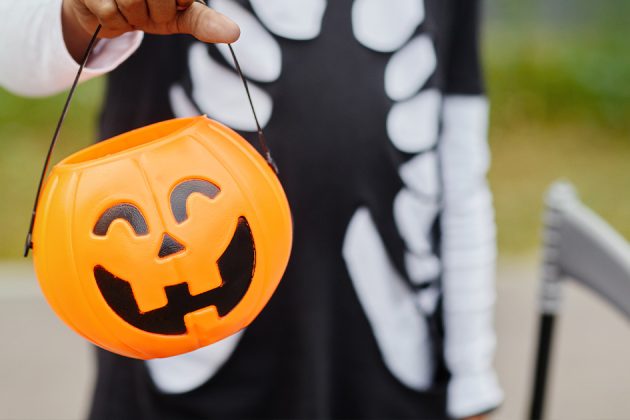 child in halloween costume holding a jack-o-lantern candy bucket