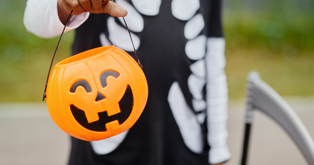 child in halloween costume holding a jack-o-lantern candy bucket