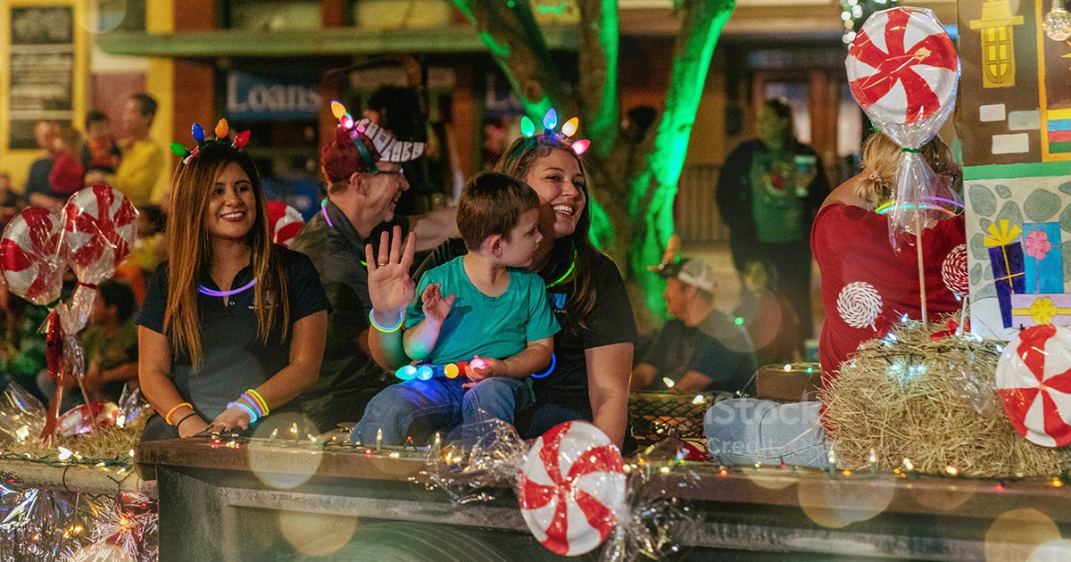 Smiling family sitting on a holiday float surrounded by lights and decorations