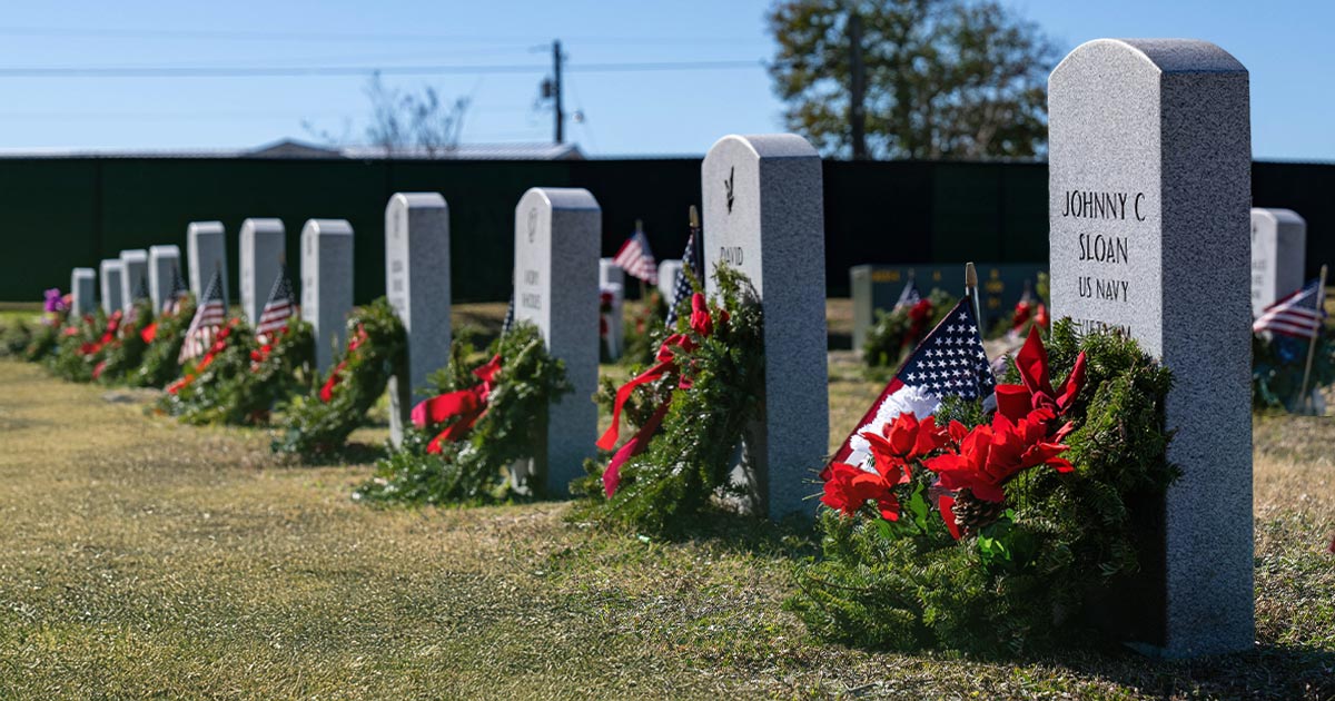 line of gravestones with holiday wreaths resting on each