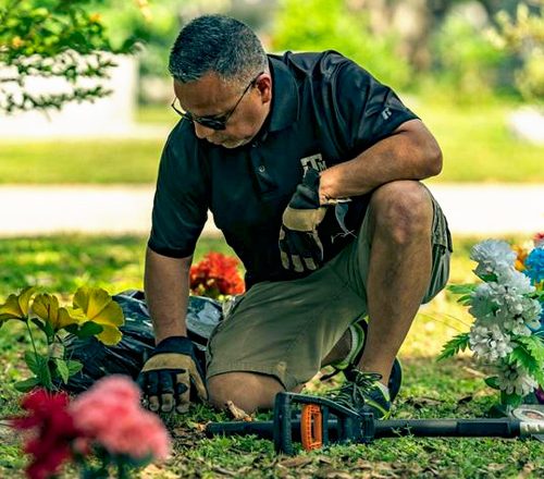 man kneeling and cleaning dirt from a headstone in a cemetery