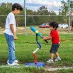 family surrounding young child practicing t-ball in a baseball field