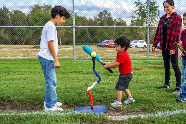 family surrounding young child practicing t-ball in a baseball field