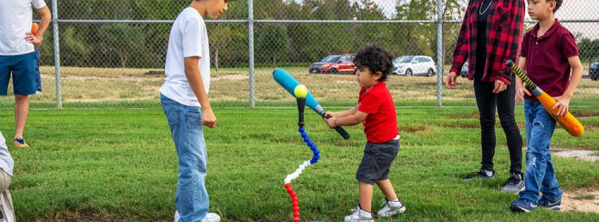 family surrounding young child practicing t-ball in a baseball field