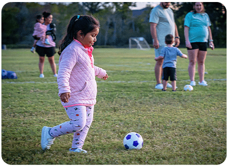 young girl kicking a mini soccer ball across a field